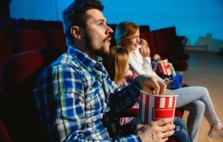 Young caucasian family watching a film at a movie theater, house or cinema. Look expressive, astonished and emotional. Sitting alone and having fun. Relation, love, family, childhood, weekend time.